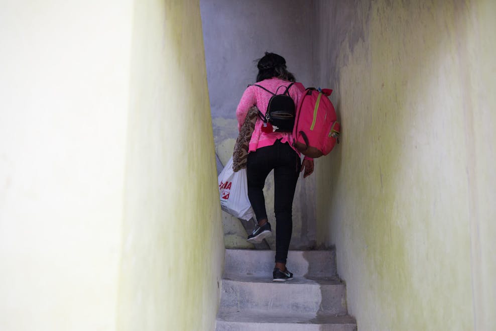 Gevolgen van seksuele uitbuiting Een meisje loopt de trap op met meerdere tassen in haar hand en op haar rug. Ze draagt een roze vest, een zwarte legging en zwarte sportschoenen.
