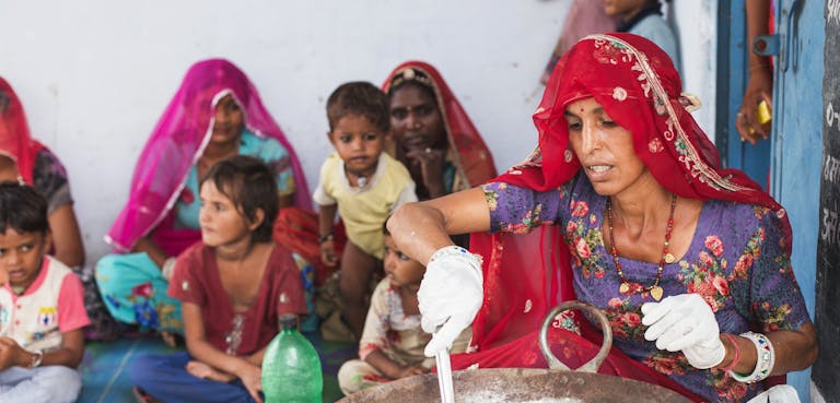 Vrouw uit India bereidt eten met kinderen op de achtergrond