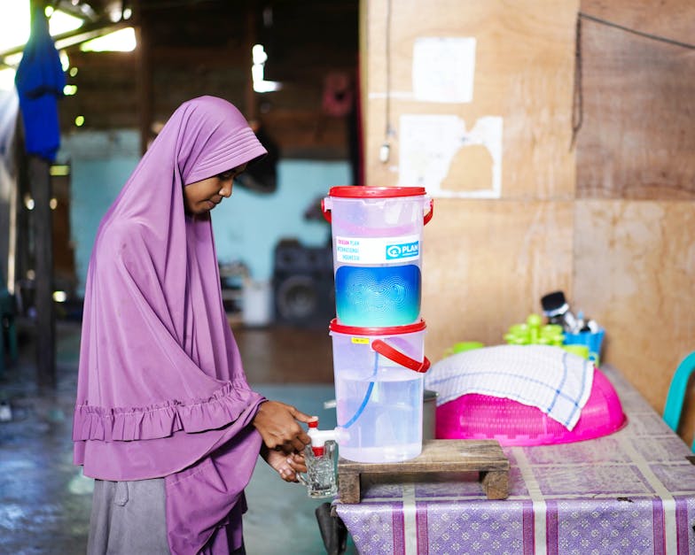 Girl uses water filter supplied by Plan International to access