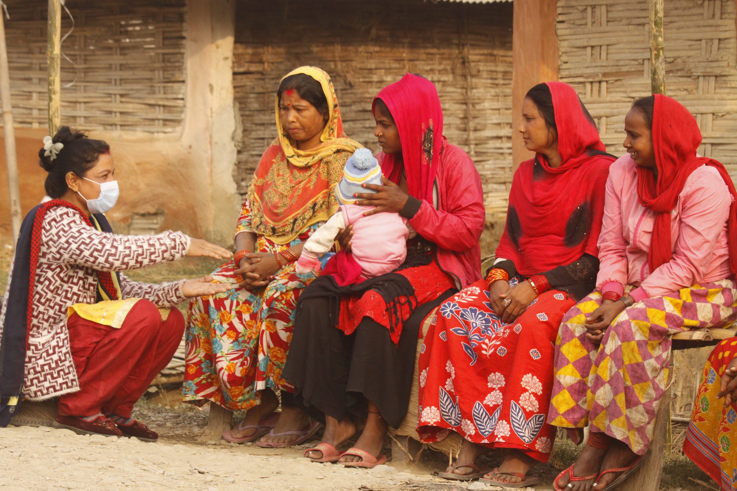 Vrouwen ontvangen corona preventie voorlichting van Plan International medewerker