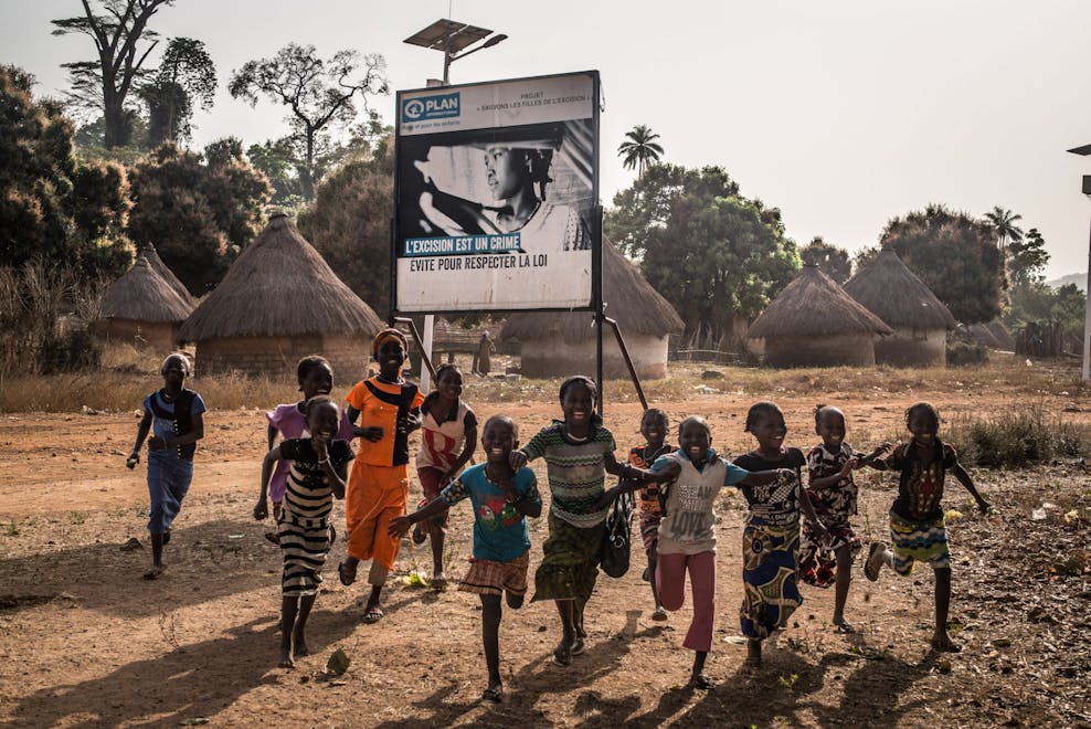 kinderen rennen langs bord van Plan International tegen FGM
