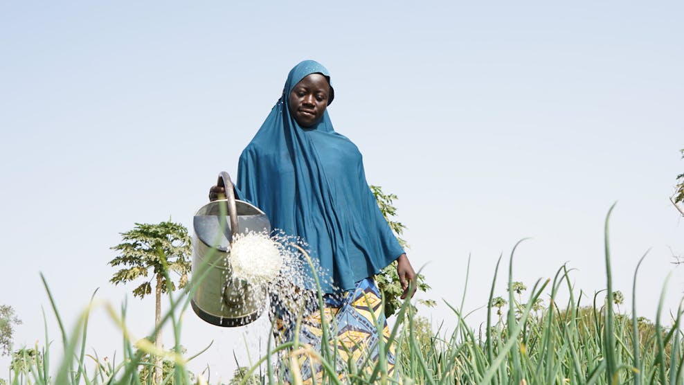 Meisje met een blauwe hoofddoek geeft met een gieter plantjes water