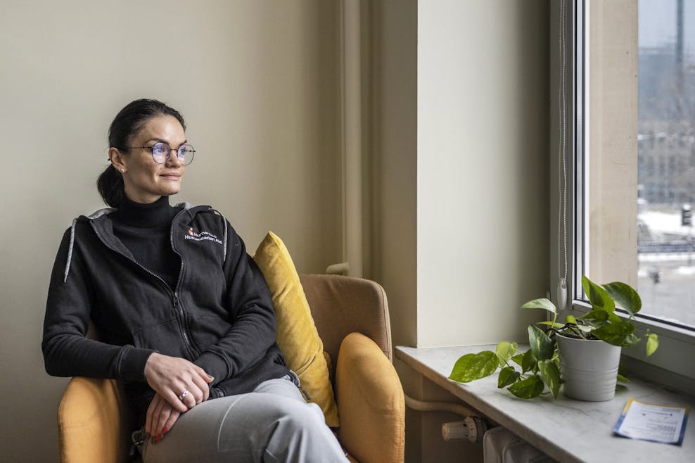 Oekraïense kinderen bouwen een nieuw leven op in Polen Een vrouw met een bril zit in een gele stoel. Ze kijkt uit het raam. Naast haar staat een plant.
