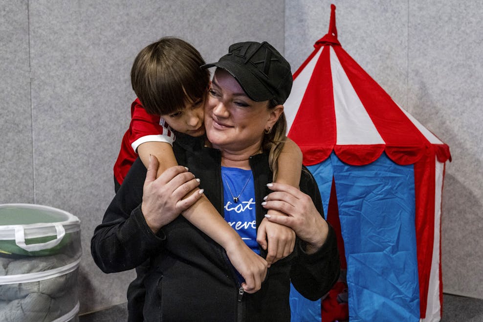 Nikita knuffelt zijn moeder Maryna. Nikita draagt een rood t-shirt. Maryna lacht, draagt een blauw shirt en een zwarte pet.