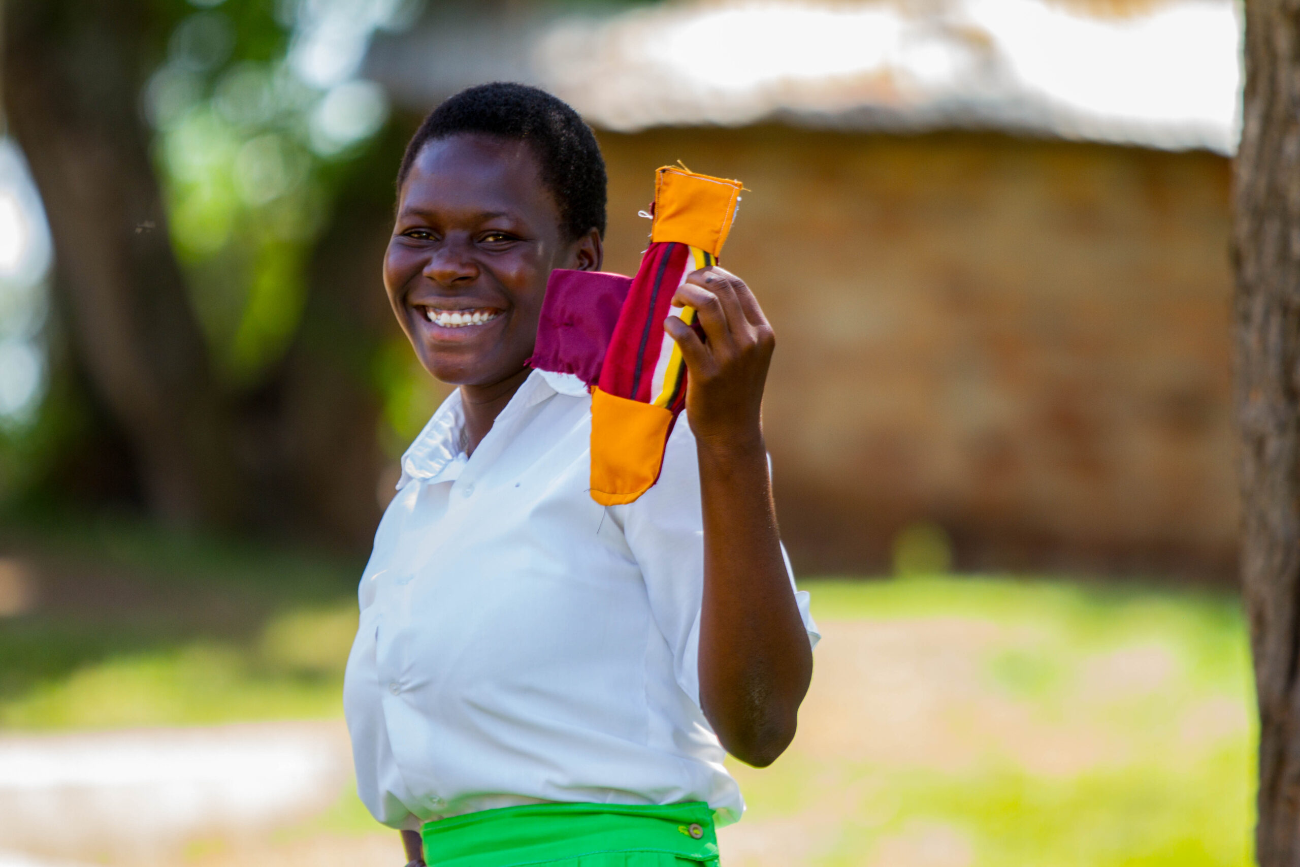 Een meisje kijkt blij in de camera. Ze houdt herbruikbaar maandverband omhoog.