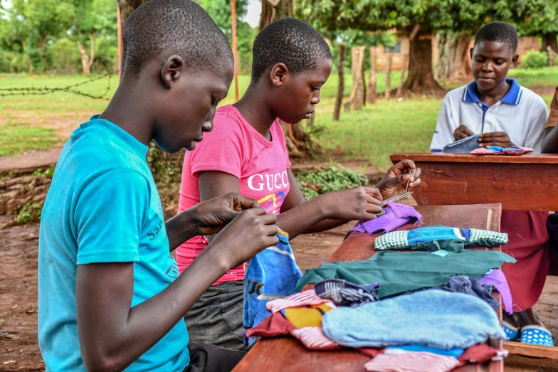 Twee jongeren zitten aan een tafel en maken herbruikbaar maandverband van kleurrijke stoffen.