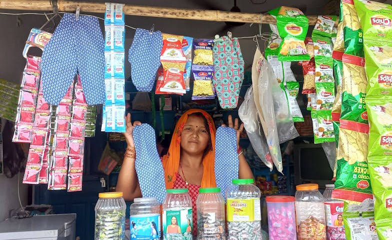 Een Nepalese vrouw staat in een kraampje met herbruikbare menstruatieproducten. In haar handen houdt ze twee stuks herbruikbaar maandverband.