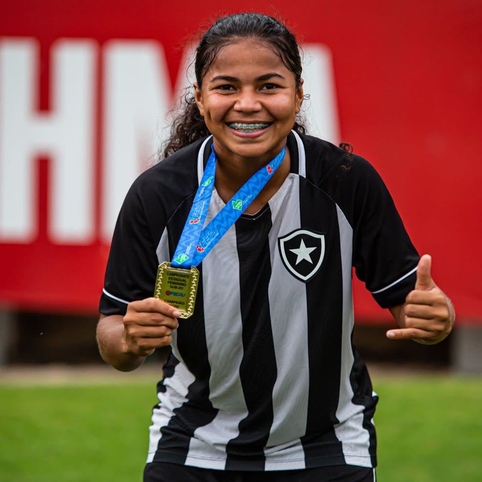 La League Meisje in voetbaltenue houdt medaille vast en lacht naar de camera