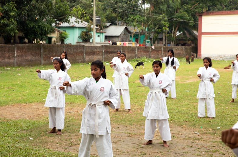 Een groep meisjes volgt karatelessen in Bangladesh. Ze dragen witte karatepakken.