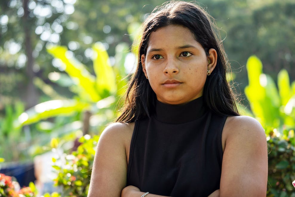 Carmen (16) kijkt in de verte. Ze heeft lang zwart haar en draagt een zwarte top.