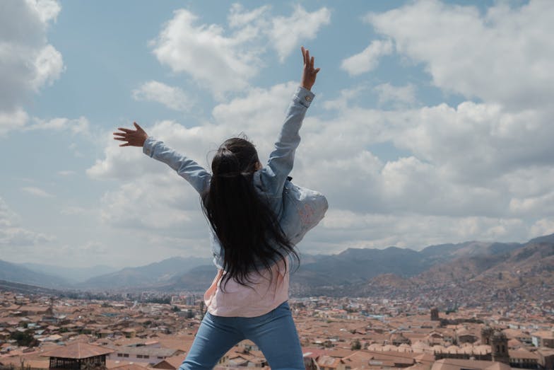 Een meisje staat met haar rug naar de camera en houdt haar handen in de lucht.