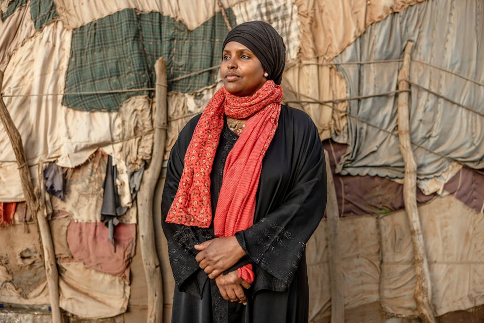 “Als meisjes de kans krijgen, schitteren ze” Een vrouw in een zwart gewaad met een zwarte hoofddoek en oranje sjaal kijkt weg van de camera.