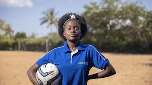 Een meisje uit Mozambique kijkt stoer in de camera. Ze draagt een blauw t-shirt en heeft een voetbal onder haar arm.