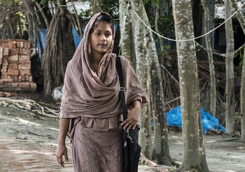 Een meisje uit Bangladesh loopt over straat. Ze draagt een roze jurk en een roze hoofddoek.