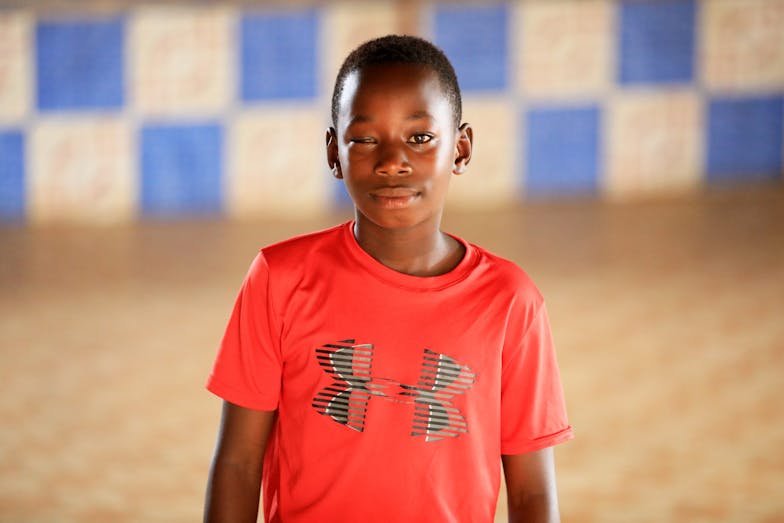 Een jongetje in een oranje t-shirt kijkt lachend in de camera.